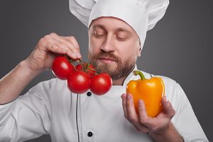 Bearded,Man,In,Chef,Uniform,Sniffing,Ripe,Tomatoes,And,Pepper