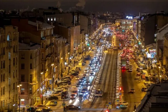 Stradă de oraș luminată seara, cu oameni care se întorc acasă